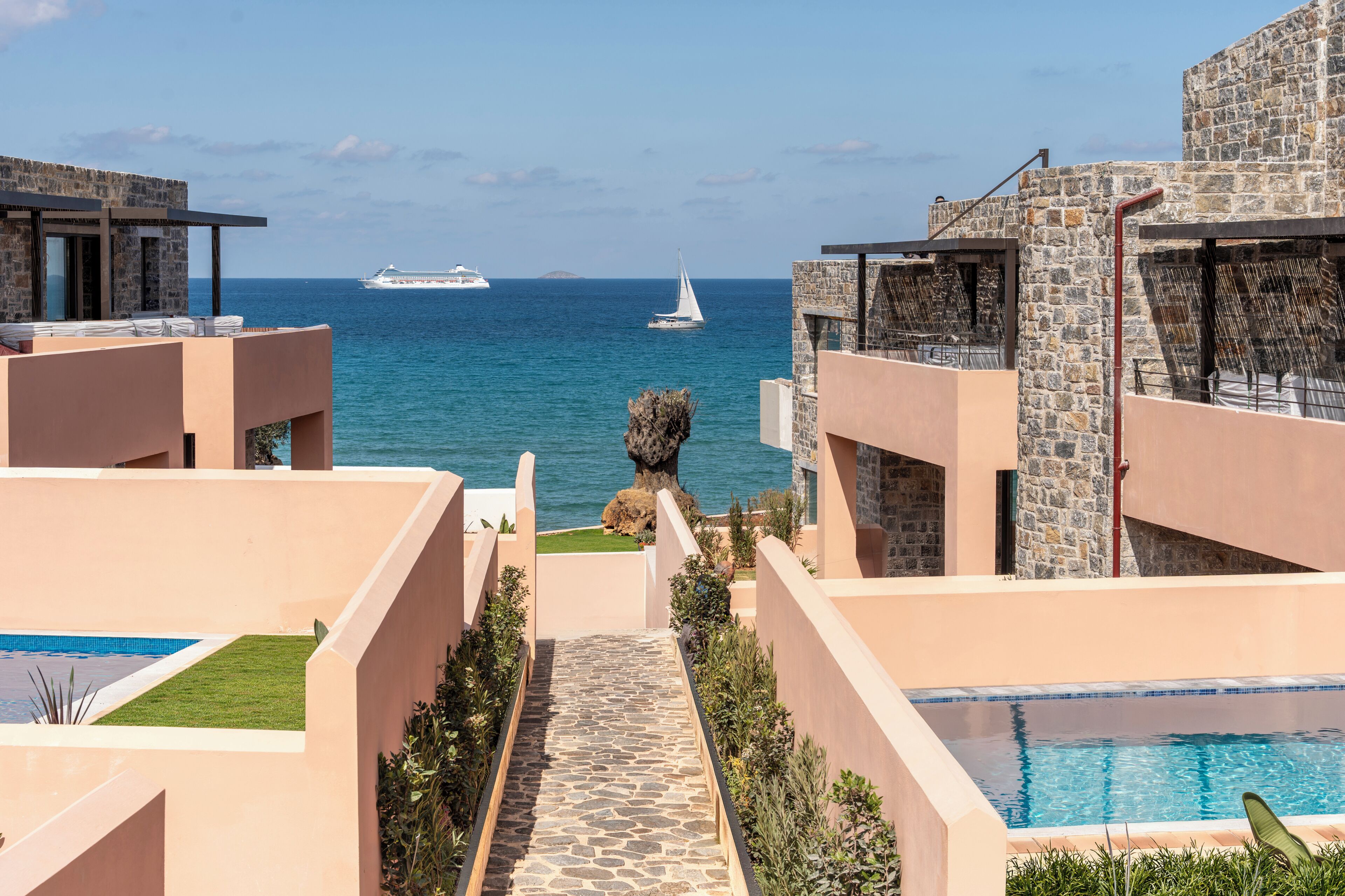A pool area with a view of the sea, a sailboat, and a cruise ship in the distance.