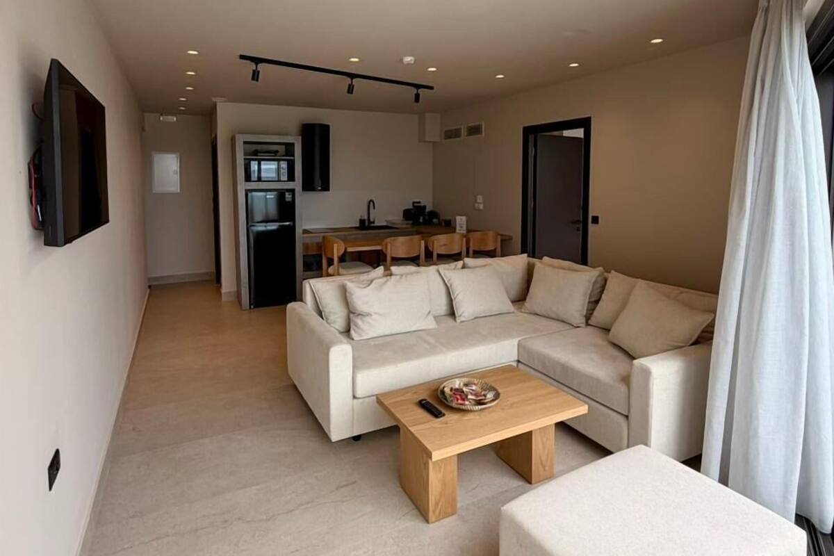 Un salon moderne avec un canapé d’angle, une table basse et un téléviseur fixé au mur.