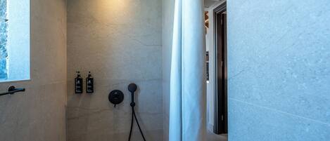 A shower with a handheld showerhead, a wall-mounted control, and two bottles of shampoo.