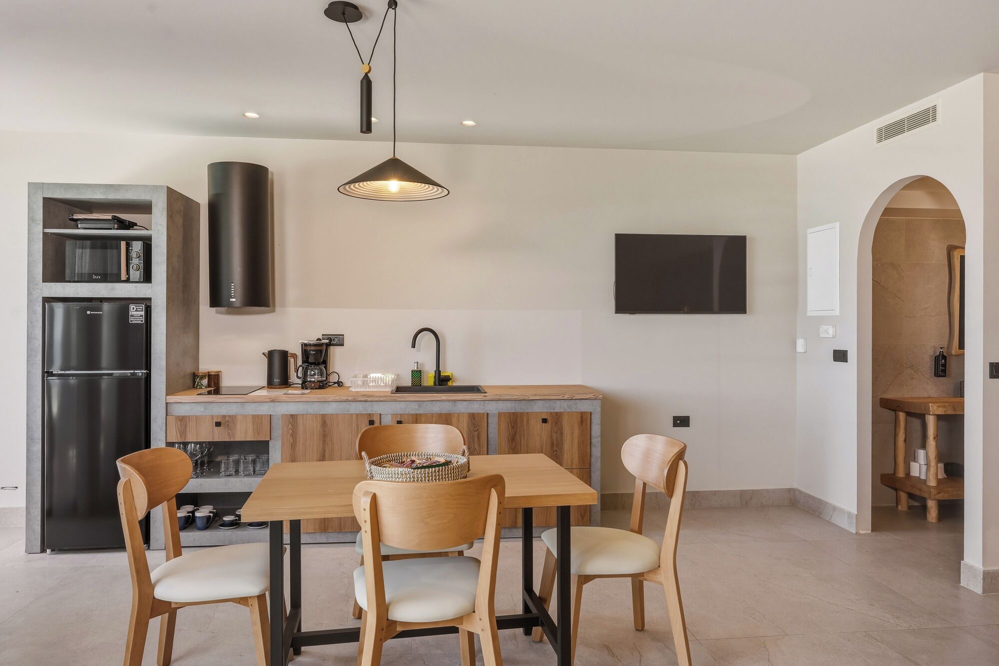 Una cocina moderna con comedor, refrigerador empotrado, cafetera y televisor montado en la pared.