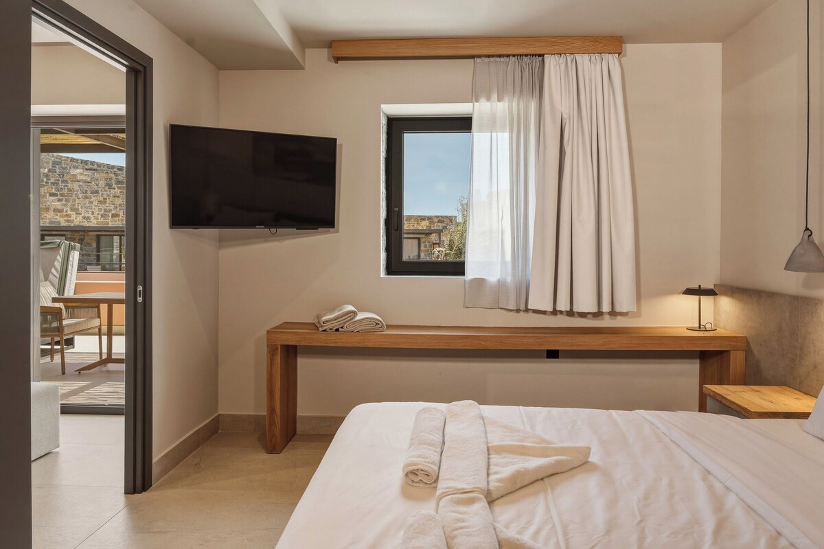 Quarto com cama, televisão, janela com cortinas, mesa de cabeceira e abajur.