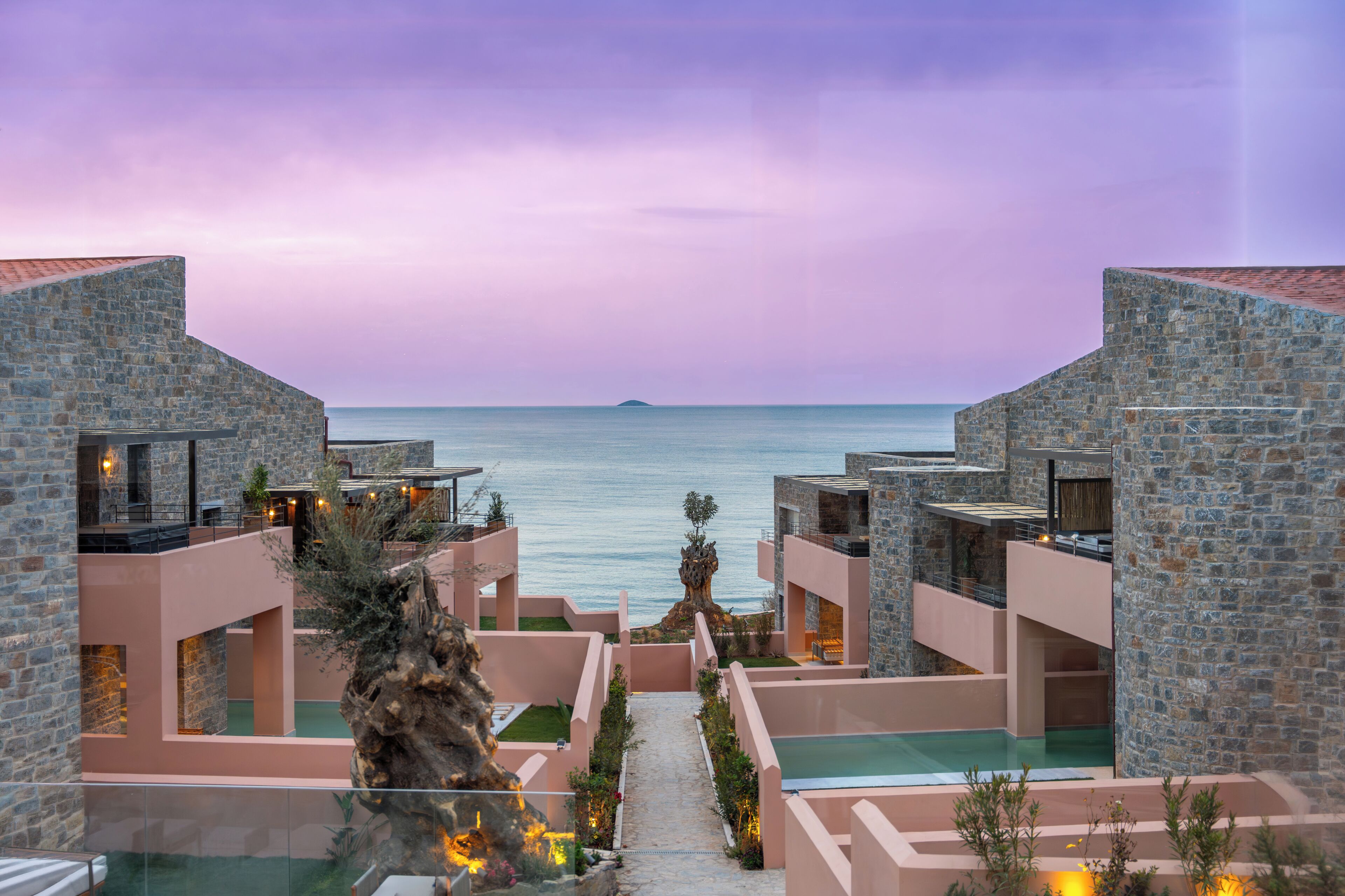 A resort with stone buildings, a pool, and a view of the sea.