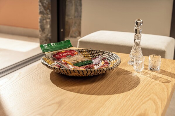 A wooden table with a woven basket containing food items, a crystal decanter, and two crystal glasses. - Volta Seaside Hotel (Hersonissos)
