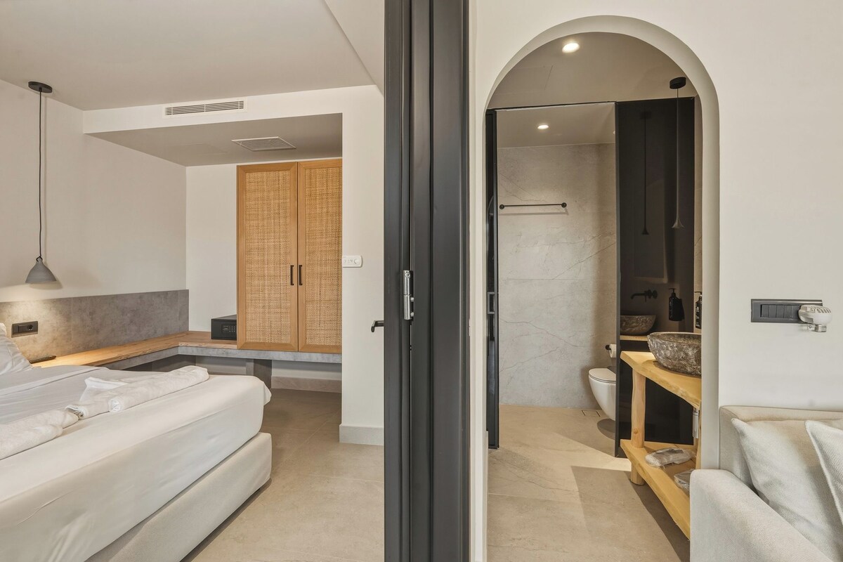 A modern bedroom with a bed, a bedside table, a wardrobe, and a bathroom visible through an archway.