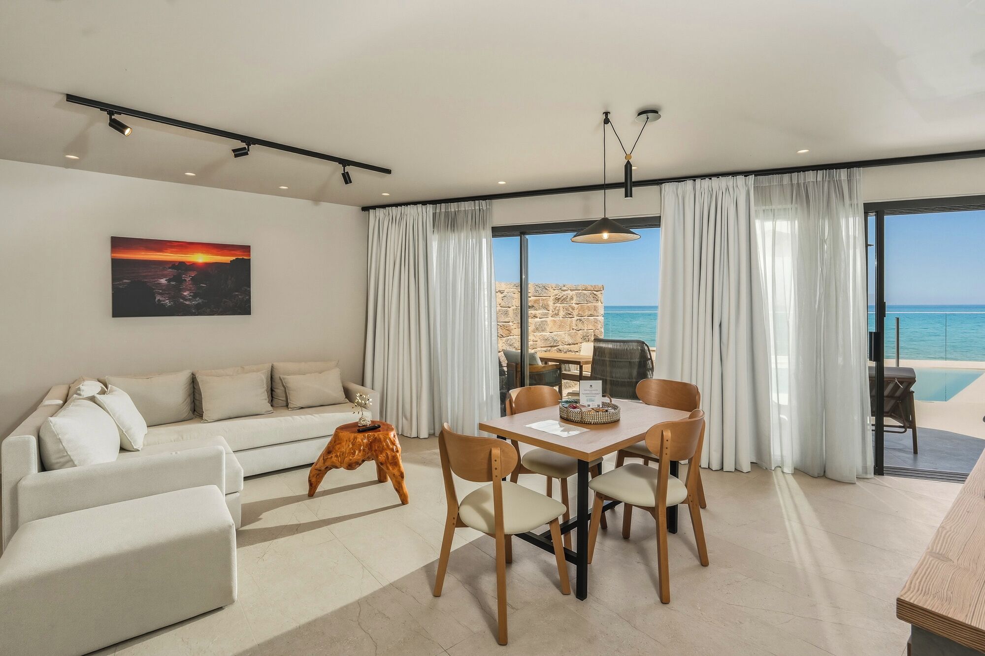 Un moderno salón con un sofá, una mesa de comedor y sillas, un cuadro en la pared y vistas al mar a través de amplios ventanales.