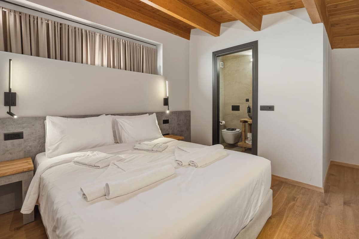 Un lit bien fait, avec du linge de lit blanc, une tête de lit en bois et un luminaire fixé au mur.
