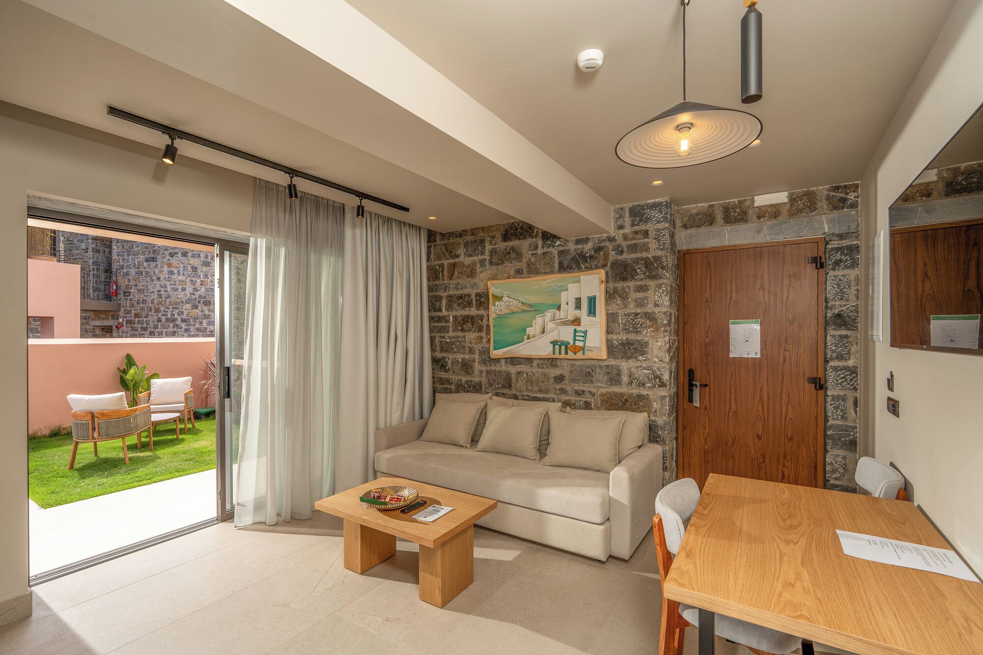A modern living room with a sofa, coffee table, and dining table. There is a stone wall and a painting on the wall.