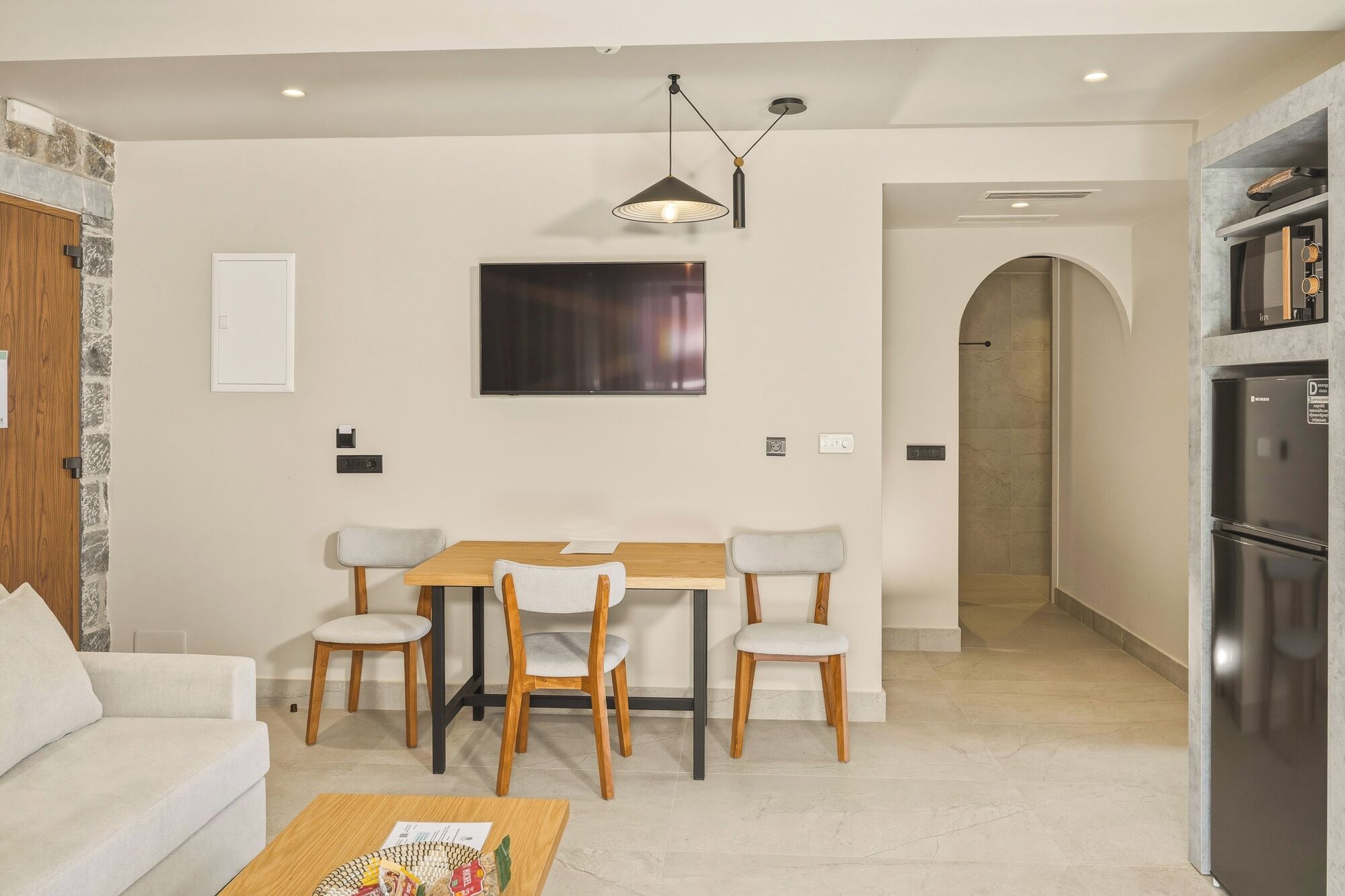 A modern living room with a sofa, a dining table with chairs, a TV, and a kitchen area with a refrigerator.