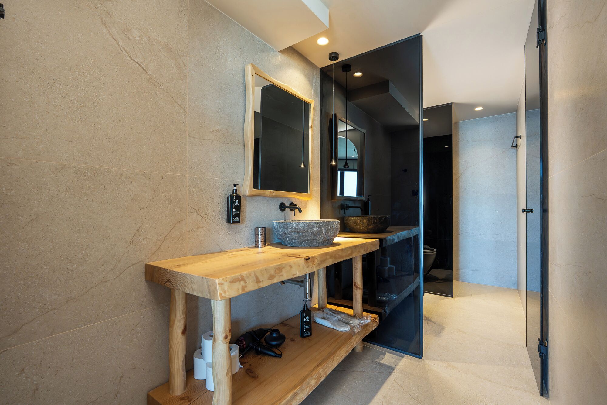 A modern bathroom with a wooden vanity, a large mirror, and a stone basin.