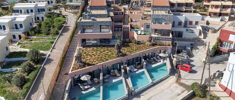 A modern hotel with a rooftop pool, multiple balconies, and a landscaped garden area.