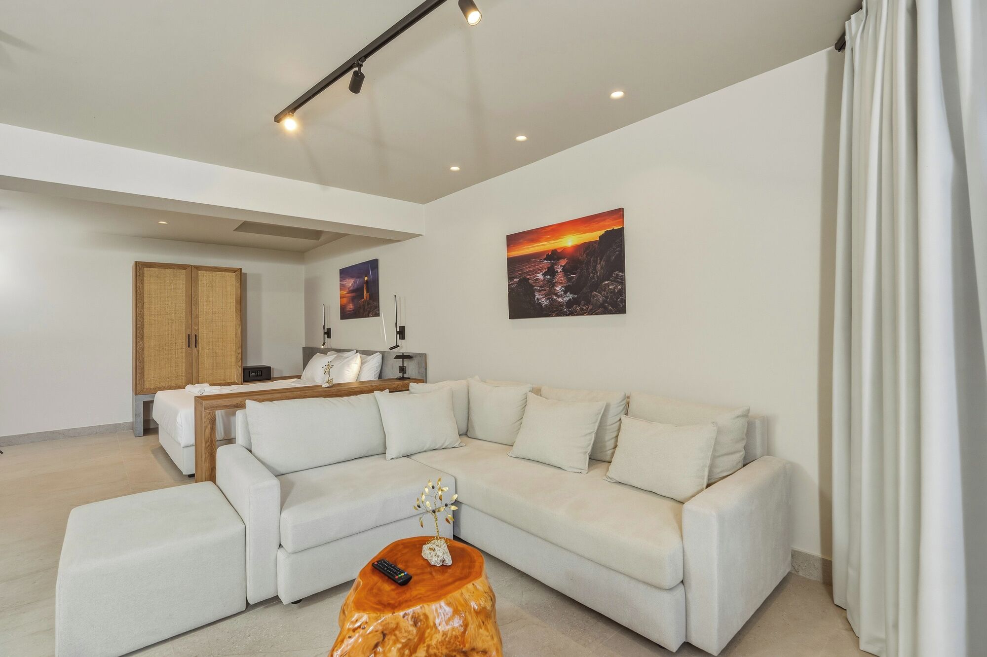 A modern living room with a sectional sofa, a wooden coffee table, and a bed with a nightstand.