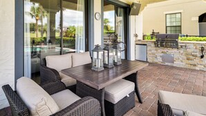 Une terrasse extérieure avec des meubles en osier, un barbecue et un mur en pierre.