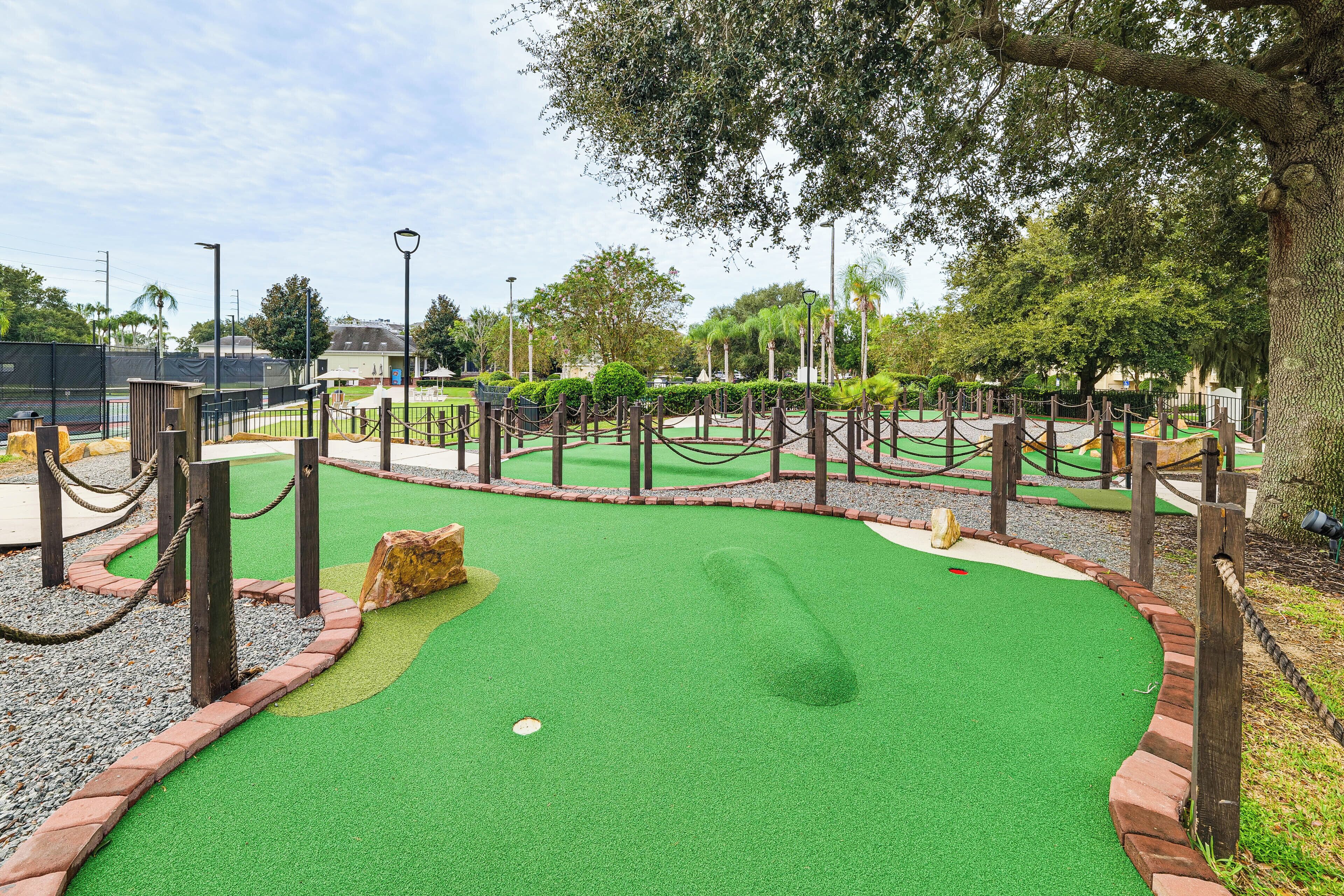 A miniature golf course with a green artificial turf, wooden obstacles, and a brick border.