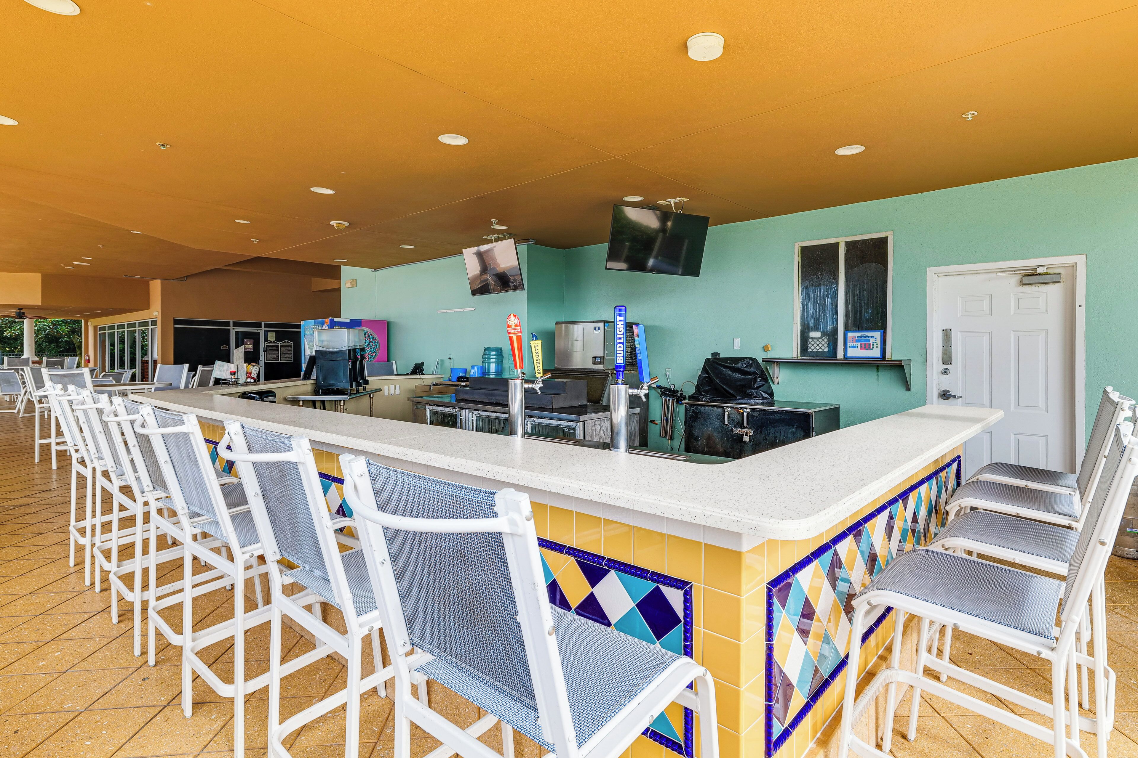 A bar area with white bar stools, a counter with a tiled backsplash, and a television mounted on the wall.