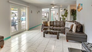 A spacious living room with a leather sofa, a glass coffee table, and a view through glass doors to an outdoor area. - Canal-front, Pet-friendly Cape Coral Retreat! (Cape Coral)