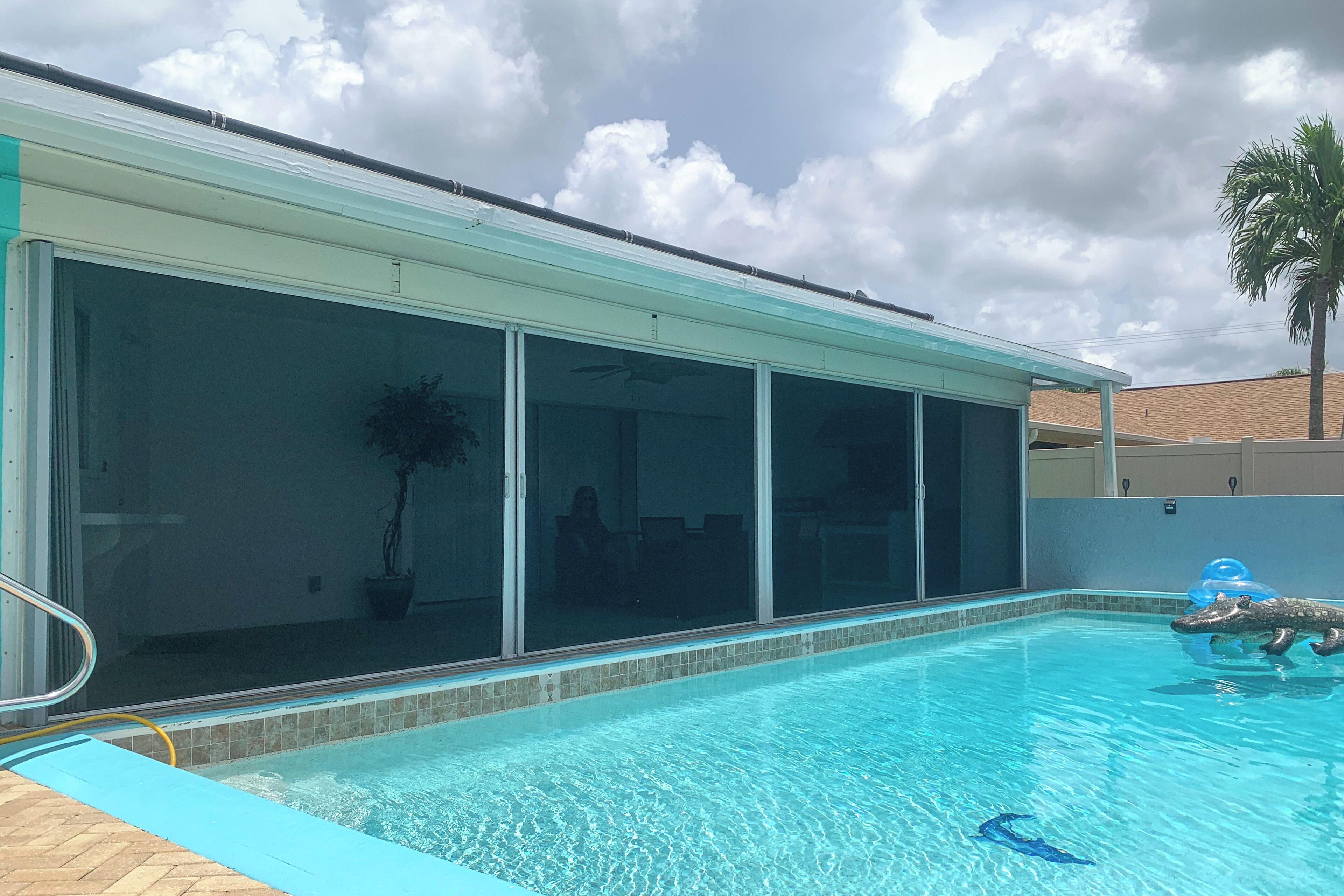 Ein Schwimmbecken mit Glasüberdachung, eine Palme und ein klarer Himmel.