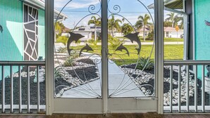 A door with a decorative metal design and a view of a landscaped garden with palm trees and a pathway. - Canal-front, Pet-friendly Cape Coral Retreat! (Cape Coral)