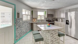 A modern kitchen with a central island, stainless steel appliances, and a view of the city through the window. - Canal-front, Pet-friendly Cape Coral Retreat! (Cape Coral)
