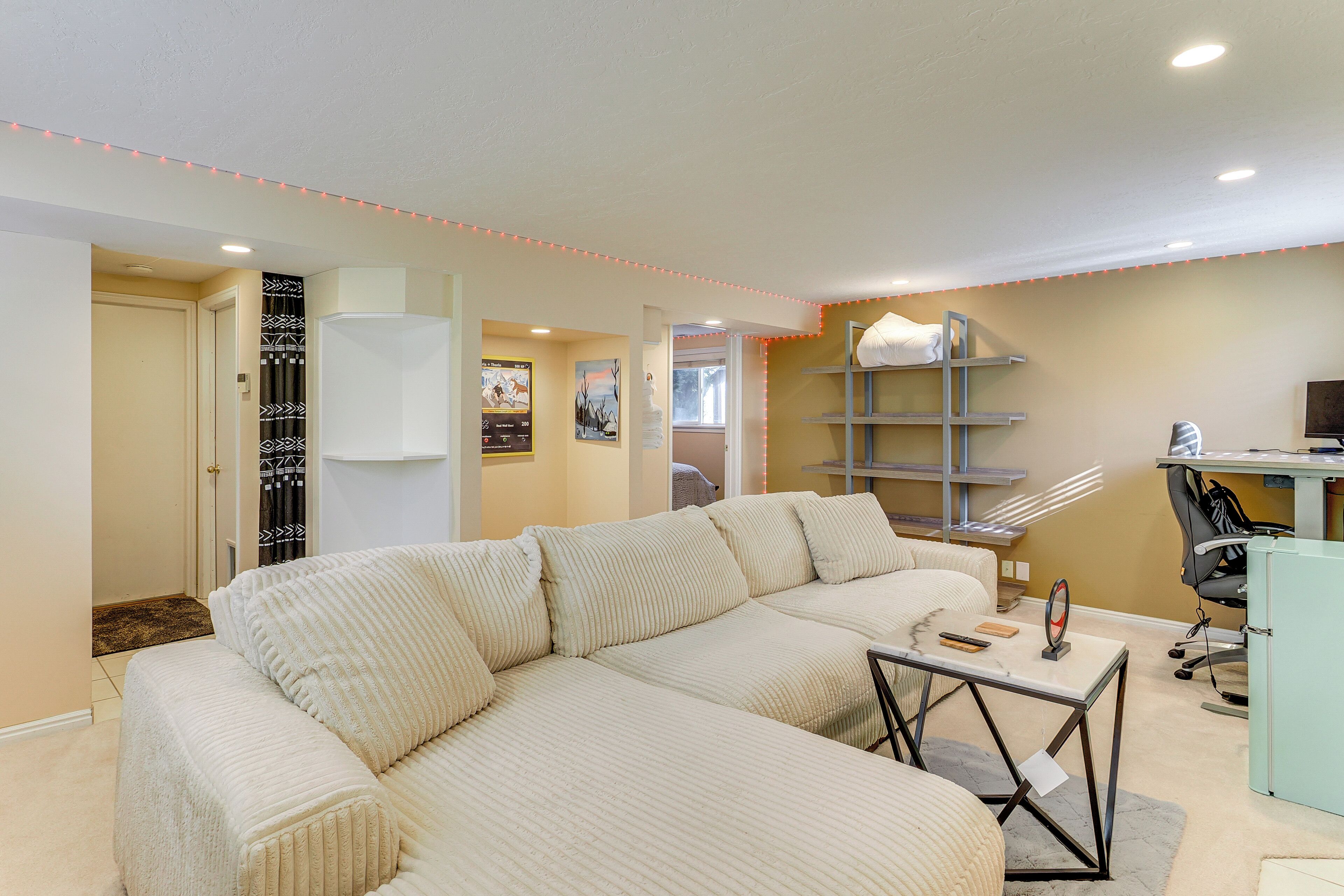 A living room with a sectional sofa, a desk with a computer, and a shelving unit.