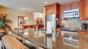 A modern kitchen with granite countertops, stainless steel appliances, wooden cabinets, and a central island with bar seating. - 1 Mi to Vail Ski Resort: Condo w/ Resort Perks! (Vail)