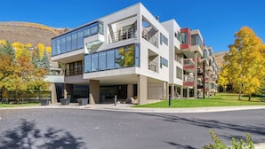 A modern multi-story building with large windows and balconies, situated in a residential area with trees and a clear sky. - 1 Mi to Vail Ski Resort: Condo w/ Resort Perks! (Vail)