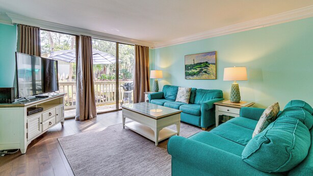 A living room with teal sofas, a coffee table, a TV, and a painting on the wall. - Walk to Beach: Peaceful Hilton Head Island Condo (Hilton Head Island)