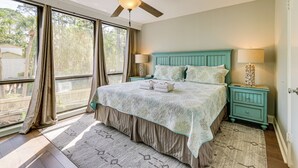 A bedroom with a bed, two nightstands, a ceiling fan, and a large window with curtains. - Walk to Beach: Peaceful Hilton Head Island Condo (Hilton Head Island)