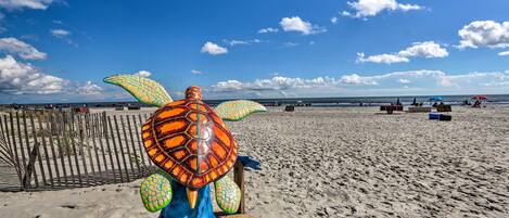 A beach scene with a large turtle sculpture in the foreground and a wooden fence in the background.