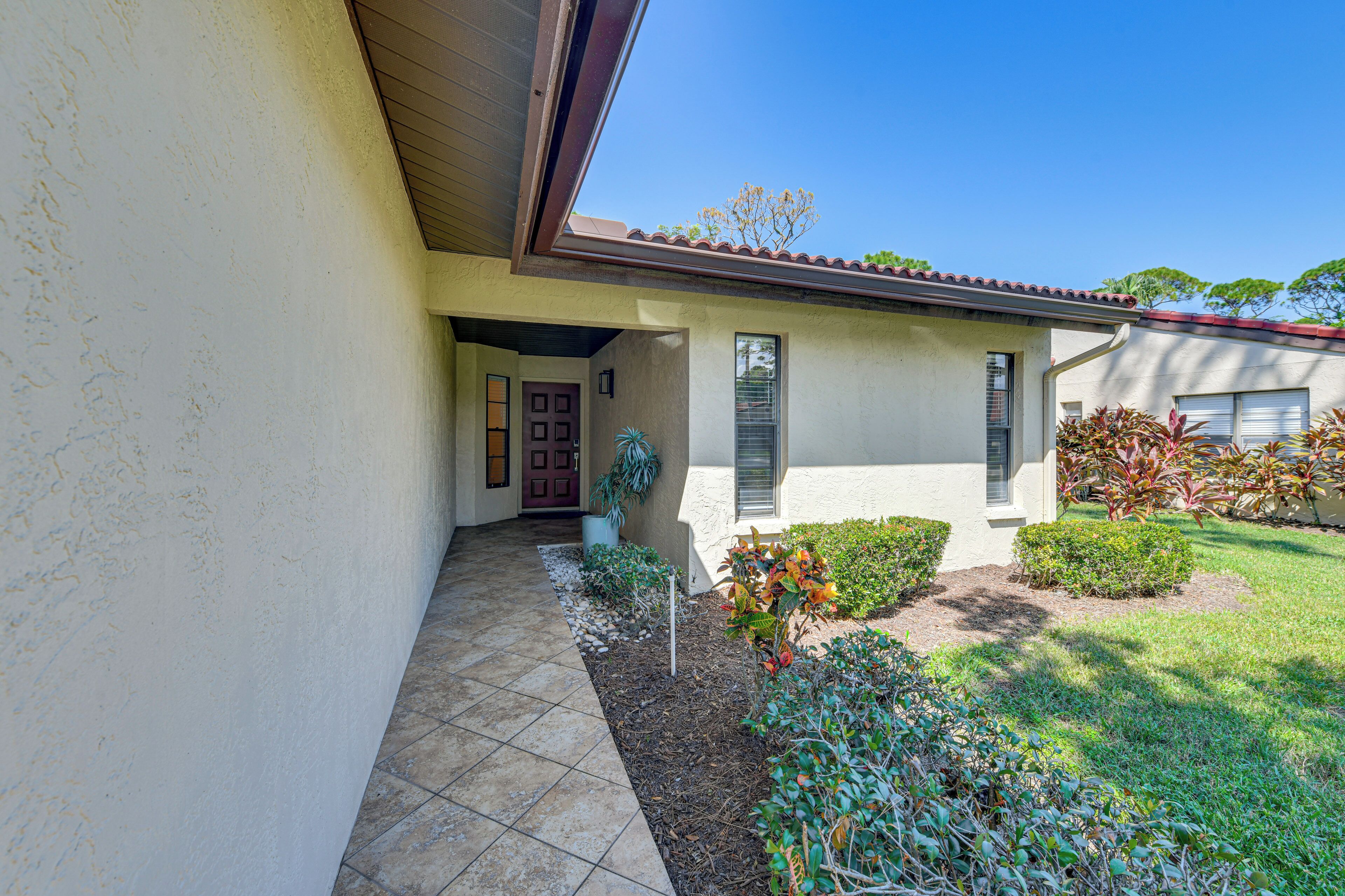 A house with a tiled entrance, a door, a window, and a small garden with plants and a tree.