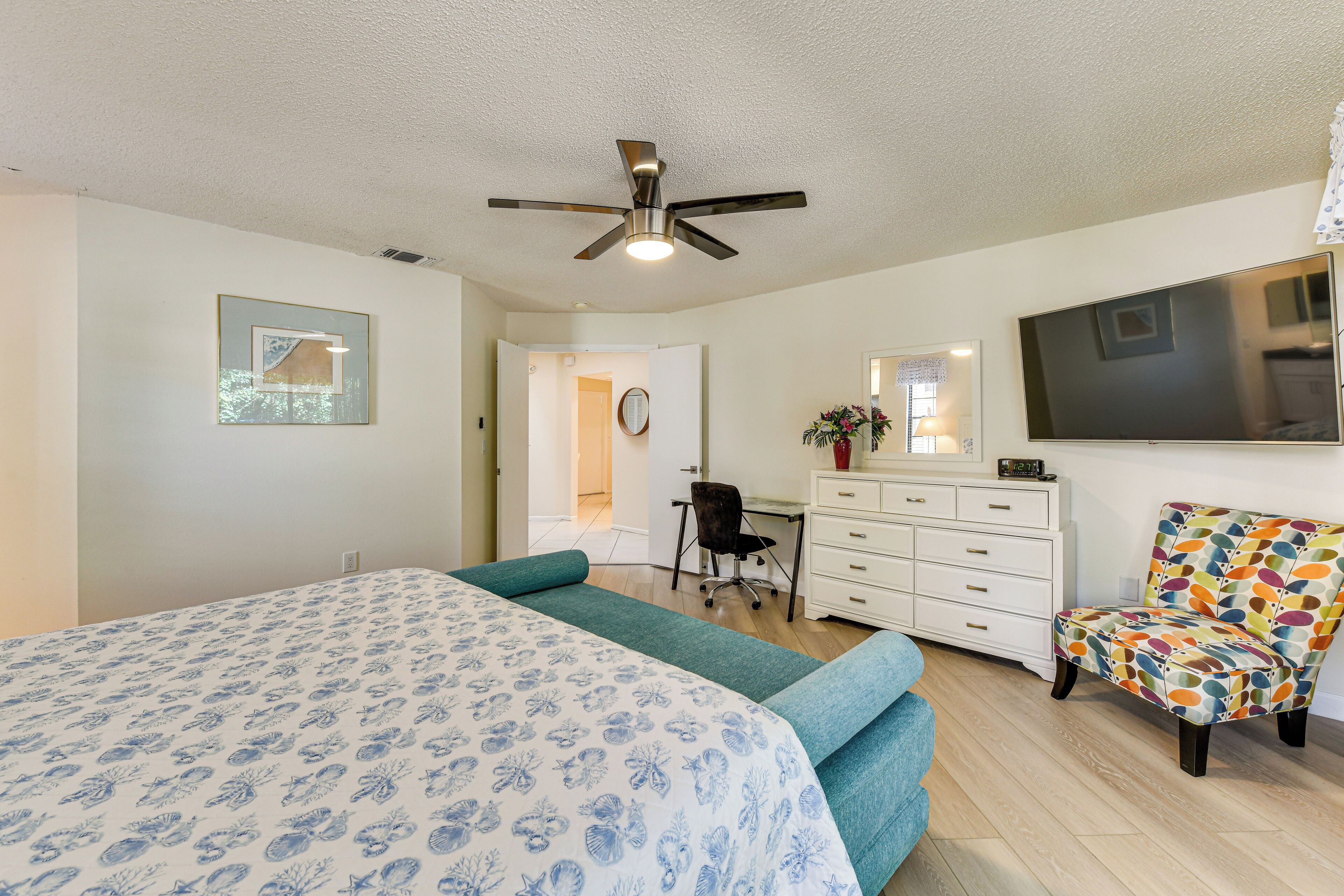 A bedroom with a bed, a desk, a chair, a dresser, and a ceiling fan.