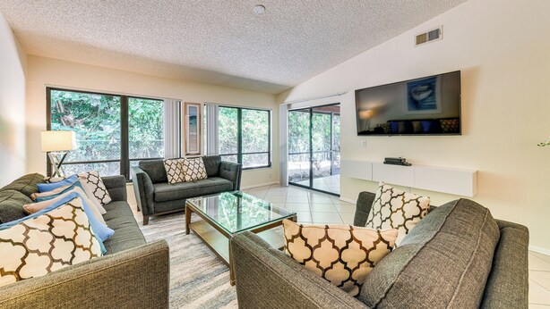 A spacious living room with a large window, a flat-screen TV, and a glass coffee table. - 4 Mi to Siesta Beach: Condo w/ Community Perks! (Sarasota)