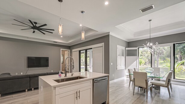 A modern kitchen with a central island, a dining area with a glass table, and a large window with blinds. - Serene Naples Home by Golf & Beaches (Naples)