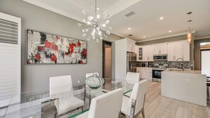 A modern kitchen with white cabinets, stainless steel appliances, and a glass dining table with white chairs. - Serene Naples Home by Golf & Beaches (Naples)
