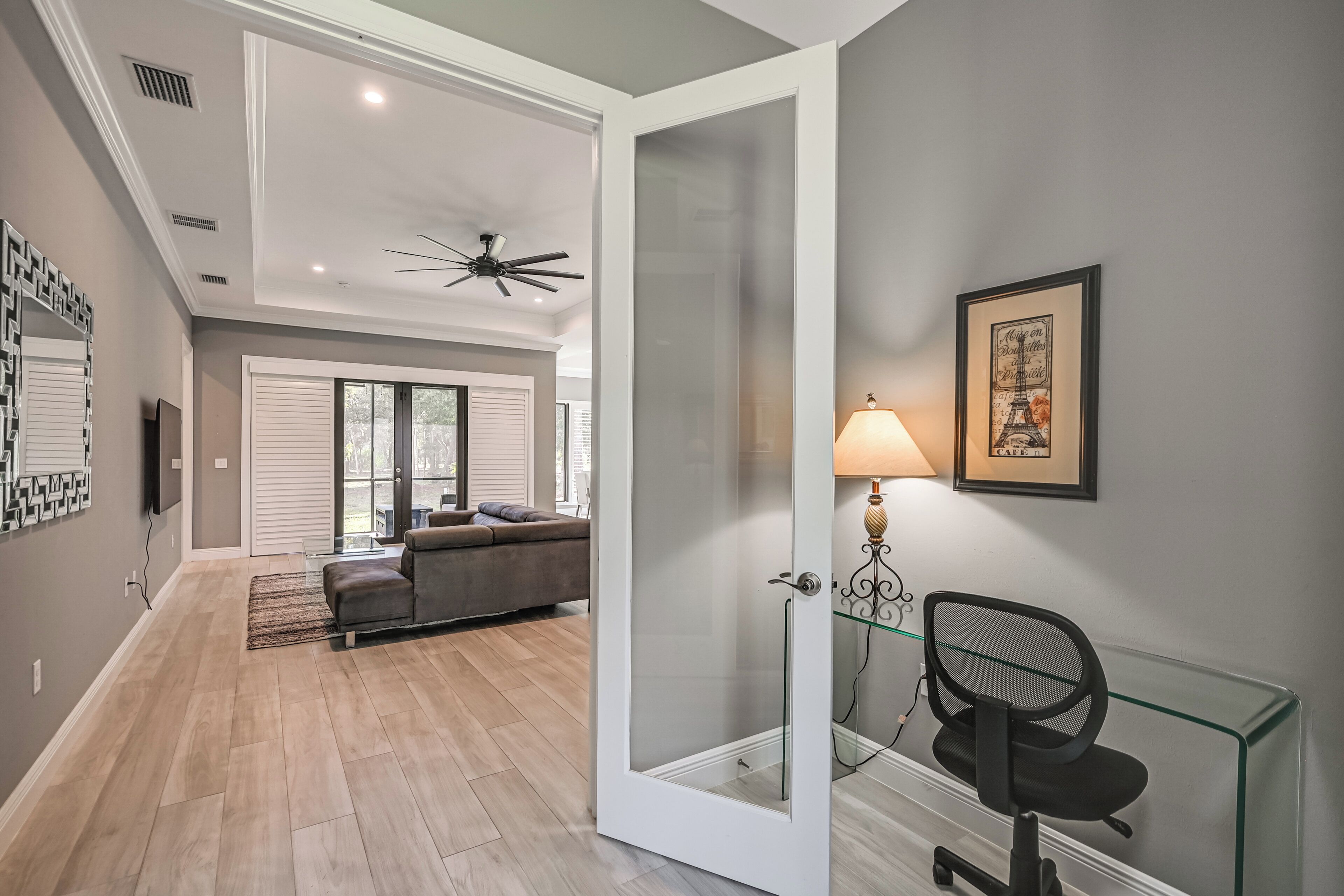 A modern living room with a glass door leading to a shower area, a ceiling fan, a framed picture of the Eiffel Tower, and a sofa with a view to the outside.