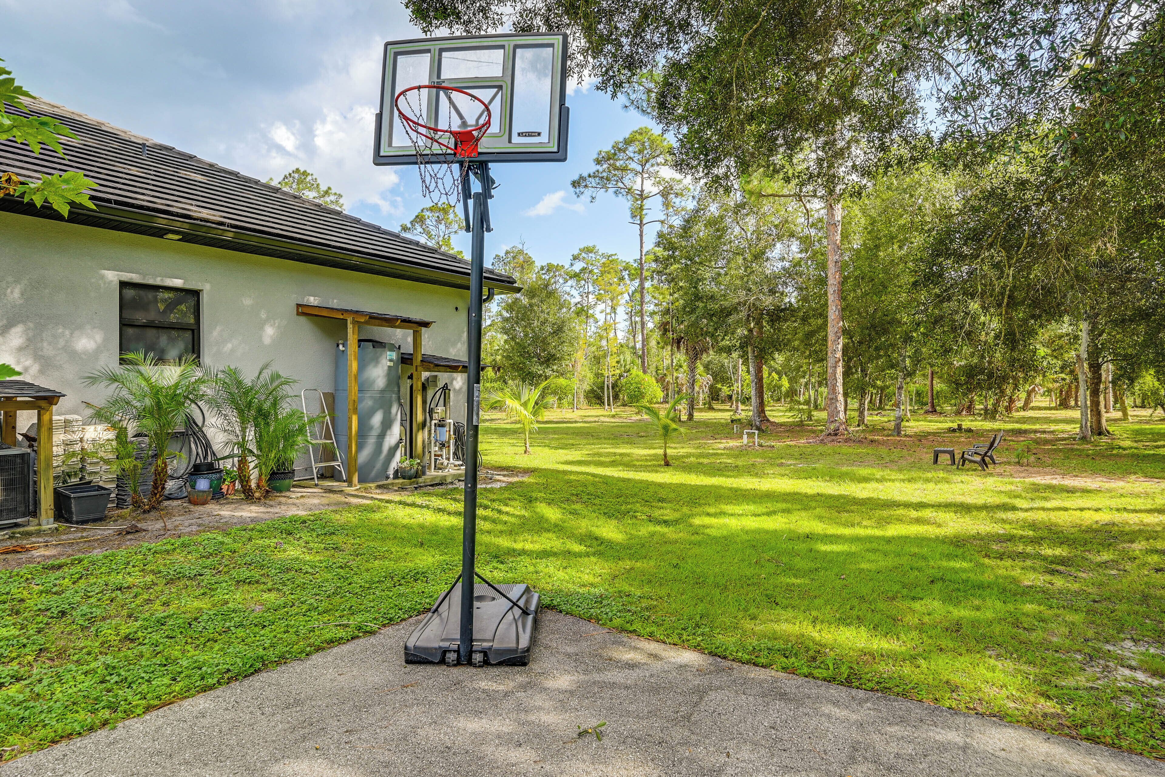 Un panier de basketball se trouve dans une zone herbeuse, avec un bâtiment en arrière-plan.