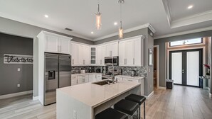 A modern kitchen with white cabinets, stainless steel appliances, and a central island with bar stools. - Serene Naples Home by Golf & Beaches (Naples)