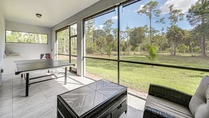 A modern room with a ping pong table, a small table, and a wicker chair. - Serene Naples Home by Golf & Beaches (Naples)
