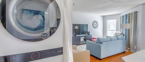A modern laundry room with a large washing machine, a sofa, and a dining area in a bright living space.