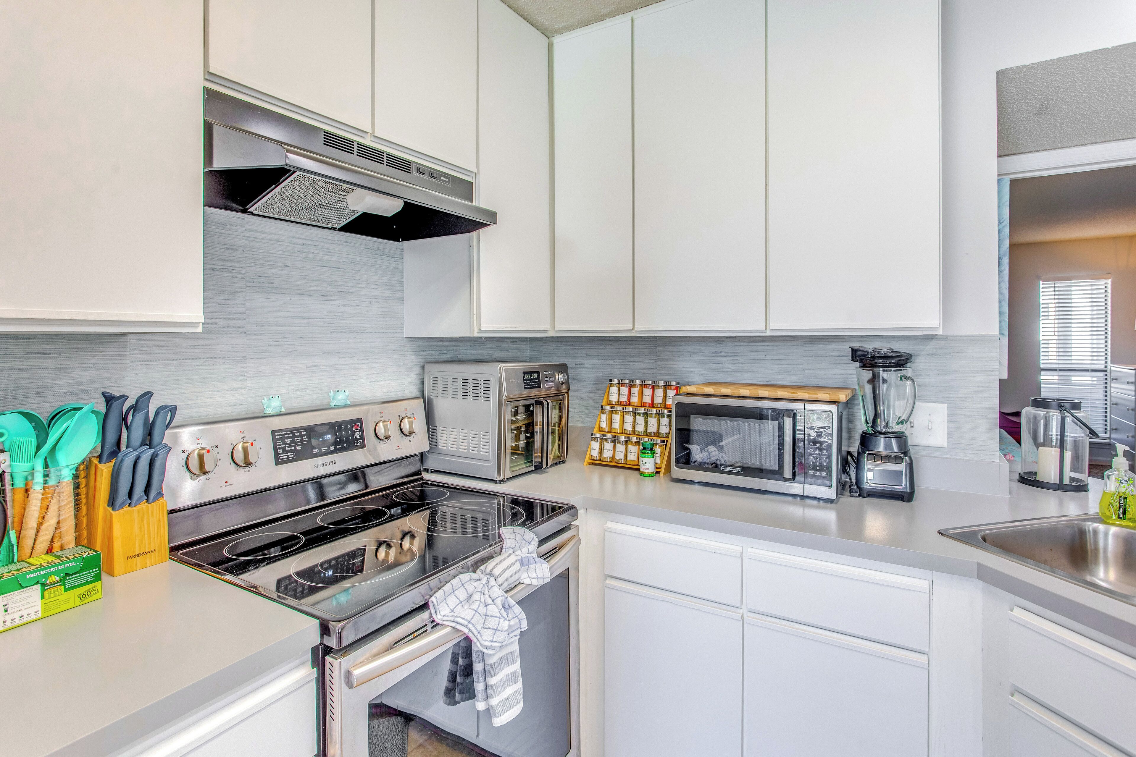 A modern kitchen with stainless steel appliances, white cabinetry, and a variety of utensils and appliances on the countertops.