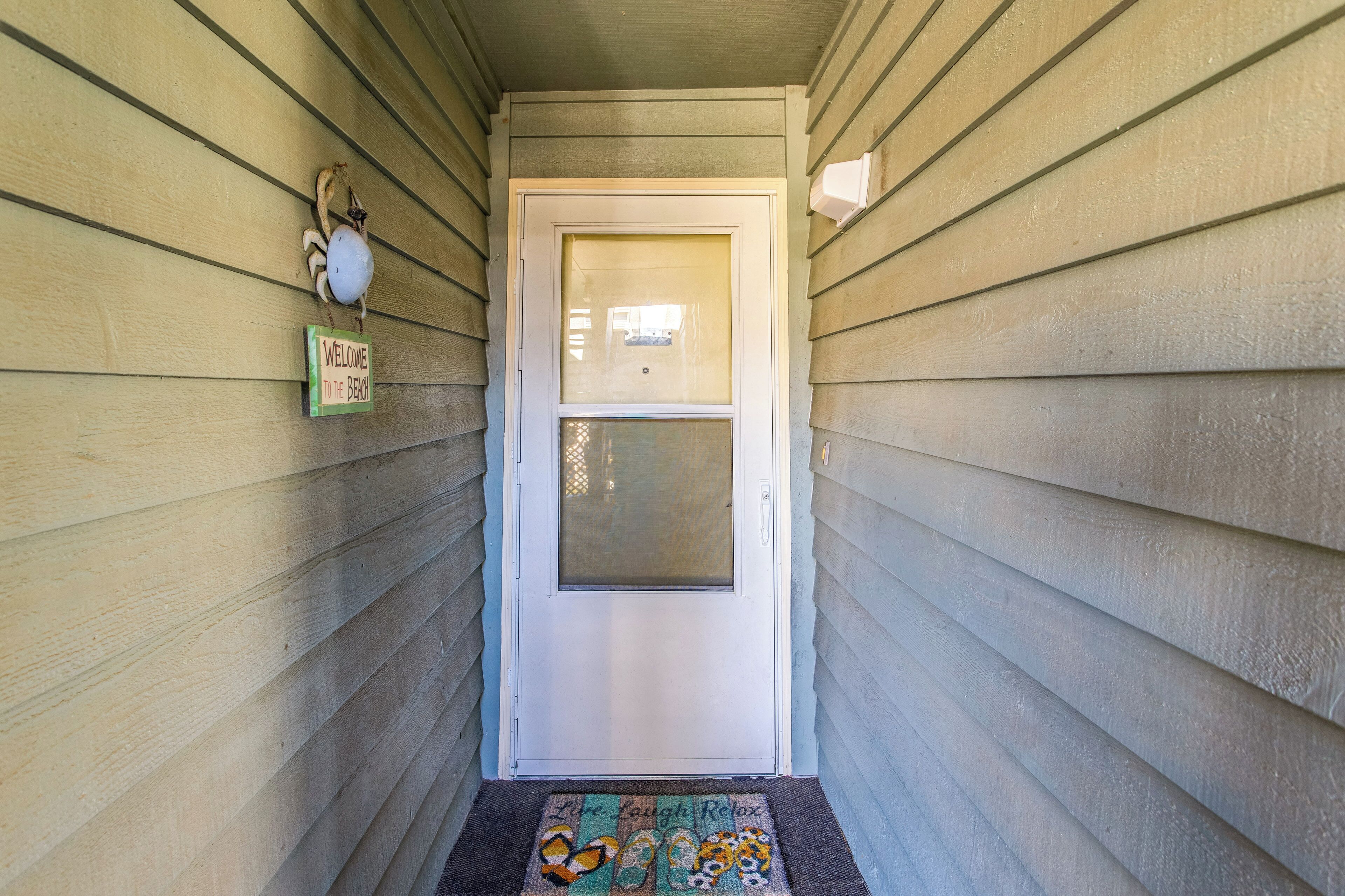 A narrow hallway with a door at the end, a welcome sign, and a doormat with a beach theme.