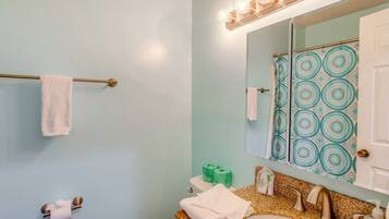 A bathroom with a light blue wall, a white sink, a mirror with a patterned shower curtain, and a towel rack.