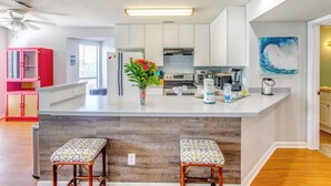 Une cuisine moderne avec des meubles blancs, un îlot central doté de tabourets, un ventilateur de plafond et une grande fenêtre.