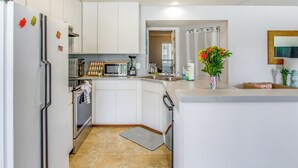 Une cuisine moderne avec des meubles blancs, un four à micro-ondes encastré, un réfrigérateur en acier inoxydable et un petit îlot central doté d’un évier.