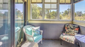 Une véranda meublée de mobilier en osier, avec une petite table et une vue sur les arbres à travers de grandes fenêtres.
