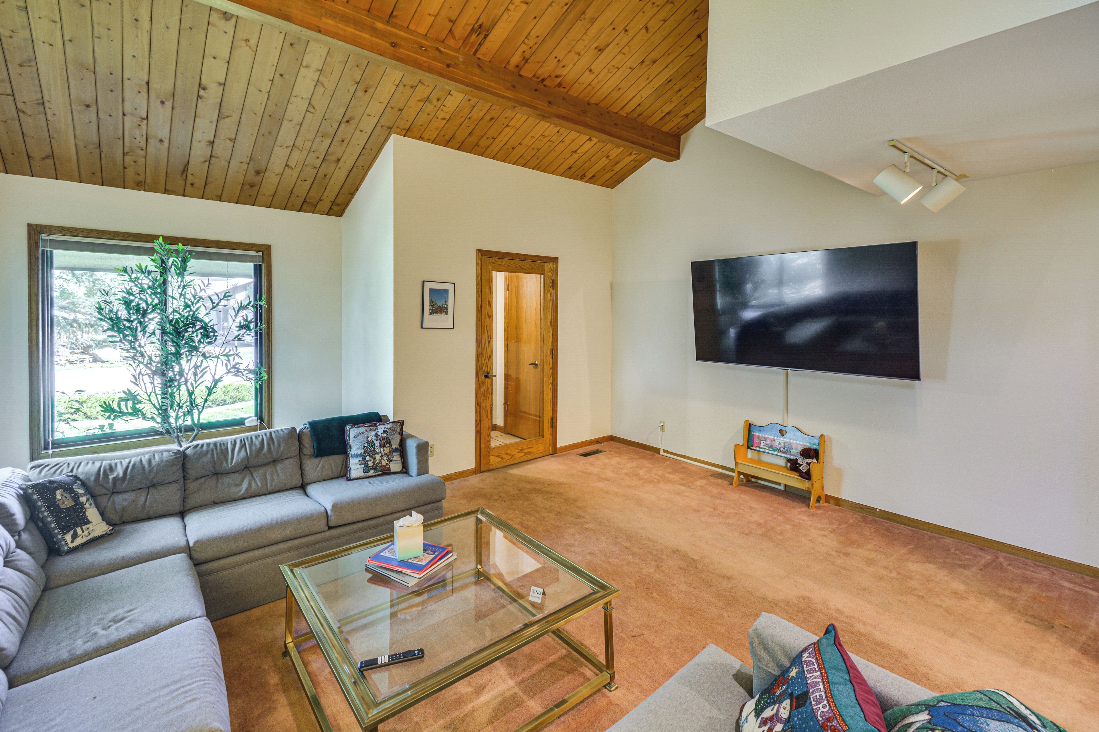 A living room with a sectional sofa, a glass coffee table, a television, and a bench with a teddy bear.