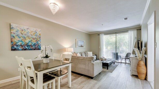 A spacious living area with a dining table, white chairs, a beige sofa, and a large window with curtains. - 2 Mi to Ocean! Poolside Escape in Miramar Beach (Miramar Beach)