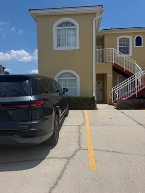 A building with a beige exterior, a staircase with red railings, and a car parked in front.
