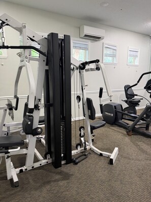 A gym with various exercise equipment, including a weight machine, an elliptical, and a stationary bike.