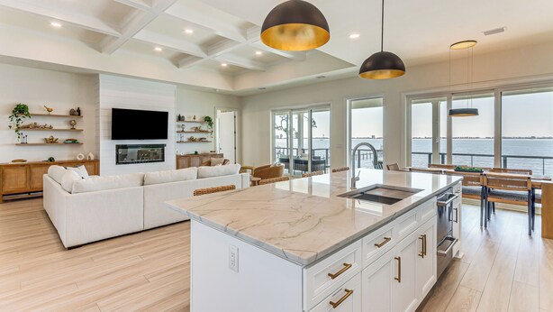 Un salón espacioso con un amplio sofá blanco, una isla de cocina con encimera de mármol e iluminación colgante.