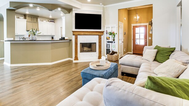 A spacious living room with a large sofa, a coffee table, and a fireplace. There is a kitchen area with white cabinets and a flat-screen TV mounted above the fireplace. - 11 Mi to Texas Tech University: Cozy Family Home! (Wolfforth)